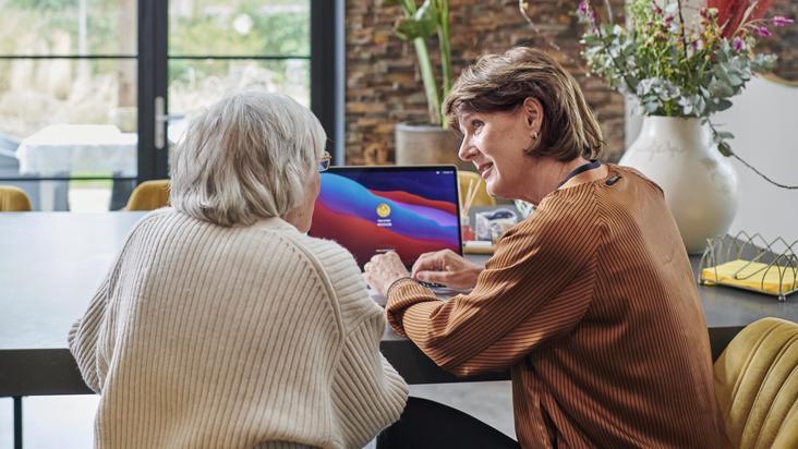 Vrouw van middelbare leeftijd en oudere vrouw in gesprek aan tafel. Beide zie je op de rug.