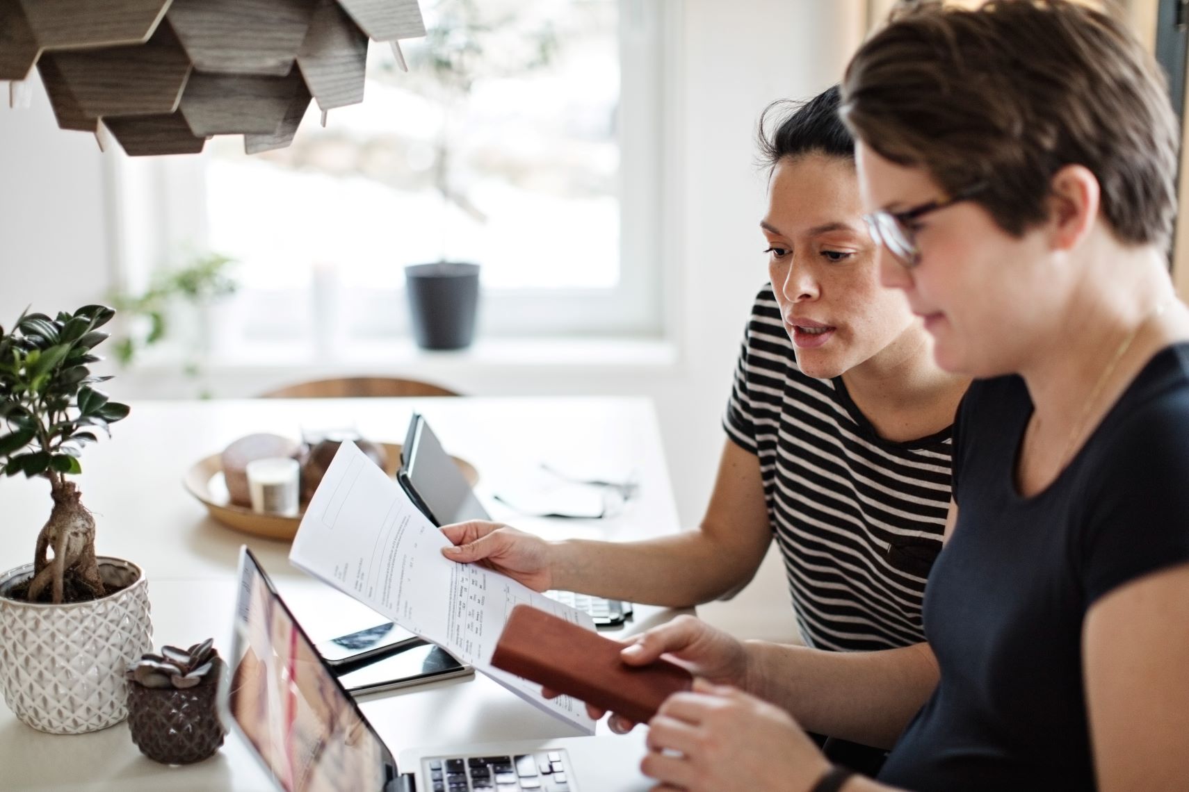 twee vrouwen doen hun bankzaken aan de tafel met bankpapieren en mobiel in de hand.