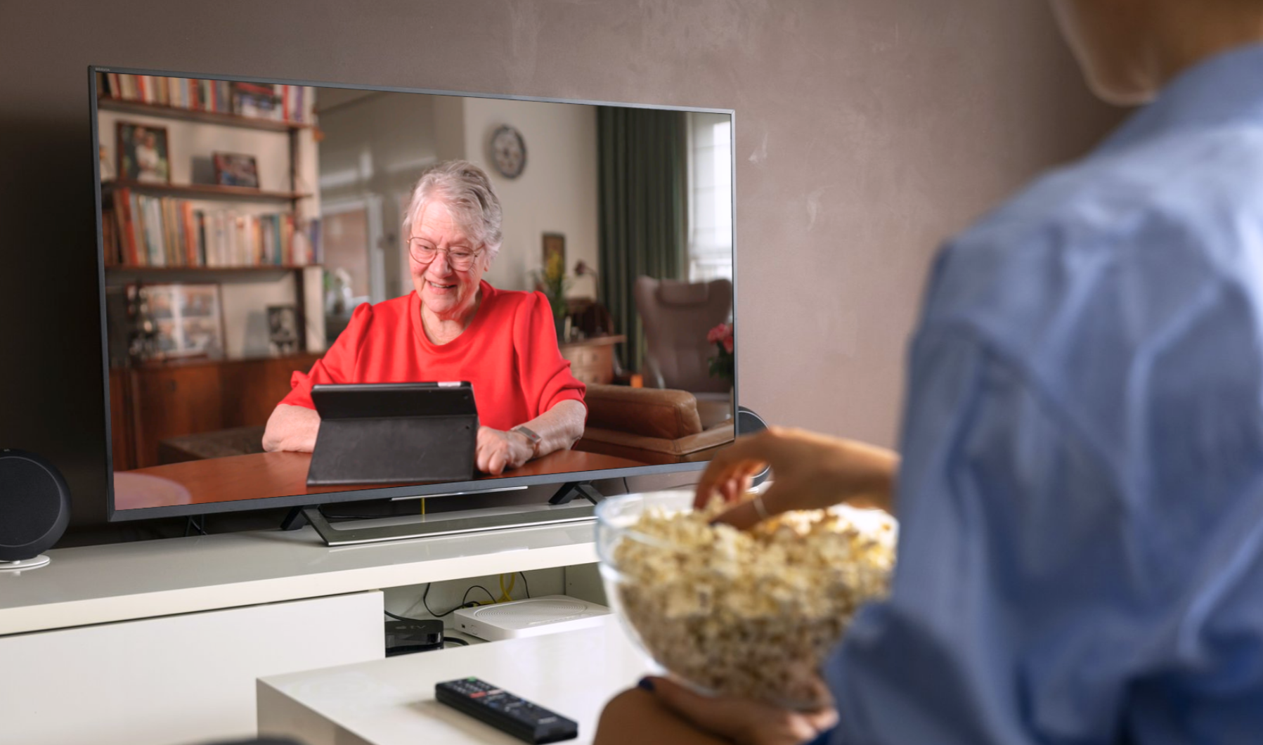 Persoon kijkt op een televisie naar de nieuwe commercial van Bankinformatiepunt, die in totaal 6 weken te zien is. In de commercial laat Anna haar oma Dory zien hoe leuk en makkelijk het is om te oefenen met bankzaken. Daarna wordt doorverwezen naar Bankinformatiepunt.nl.