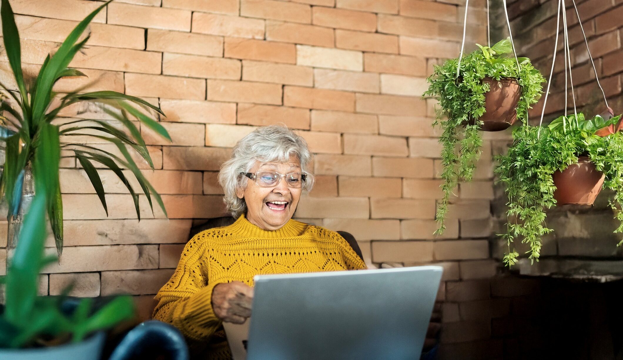 Oudere mevrouw kijkt lachend naar haar laptop terwijl ze in de tuin zit