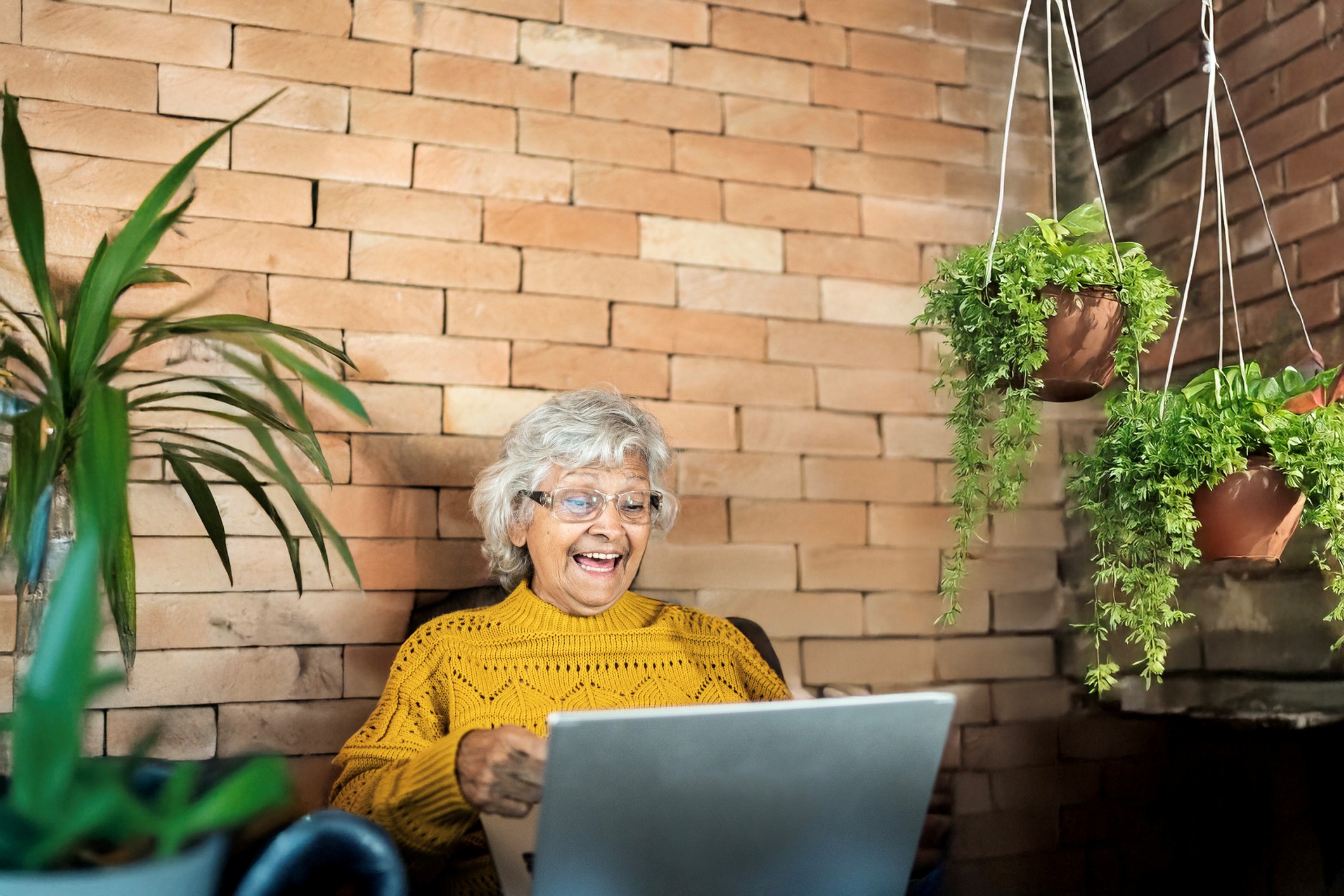 Oudere mevrouw kijkt lachend naar haar laptop terwijl ze in de tuin zit