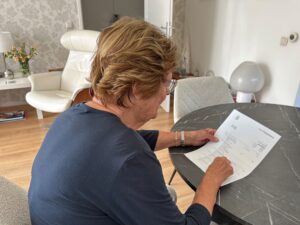 Persoon zit aan een ronde tafel in de woonkamer en controleert een papieren bankafschrift, met focus op financiële gegevens.