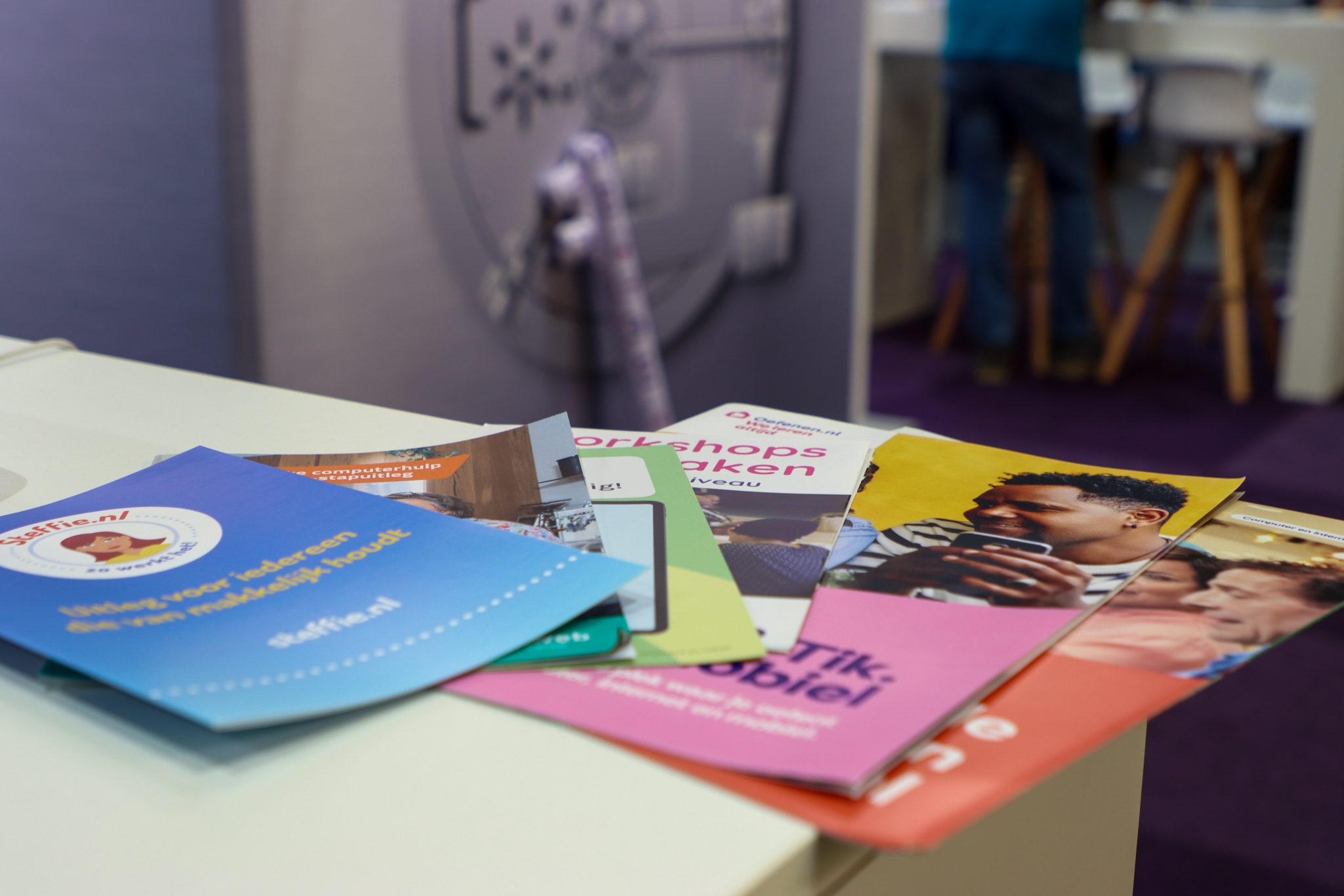 Folders en informatiefolders over digitale vaardigheden en betaalonderwerpen liggen klaar op een beursstand in een professionele ontmoetingsruimte.