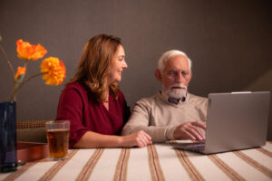 Een dochter helpt haar vader met zijn digitale bankzaken aan tafel.