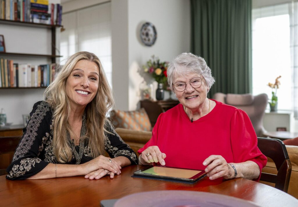 Lucille Werner met haar buurvrouw Dory aan de keukentafel terwijl ze bezig zijn met het oefenen van bankzaken.