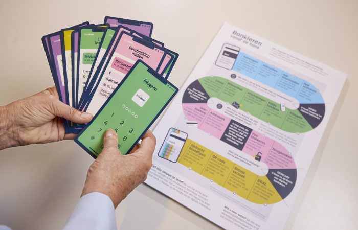 Handen houden oefenkaarten van bankhandelingen vast naast een werkblad over digitaal bankieren.